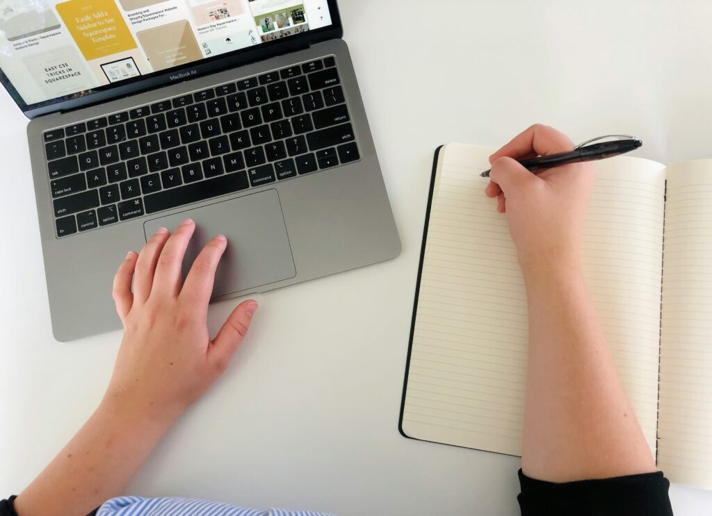 Rédacteur web travaillant sur ordinateur avec un carnet, entre intelligence artificielle et réflexion humaine